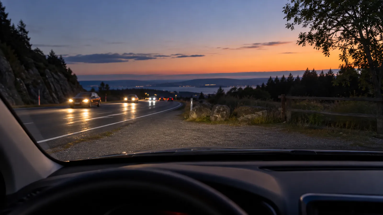 Carretera al anochecer con luces de vehículos, vista desde el interior de un coche detenido en un apartadero.